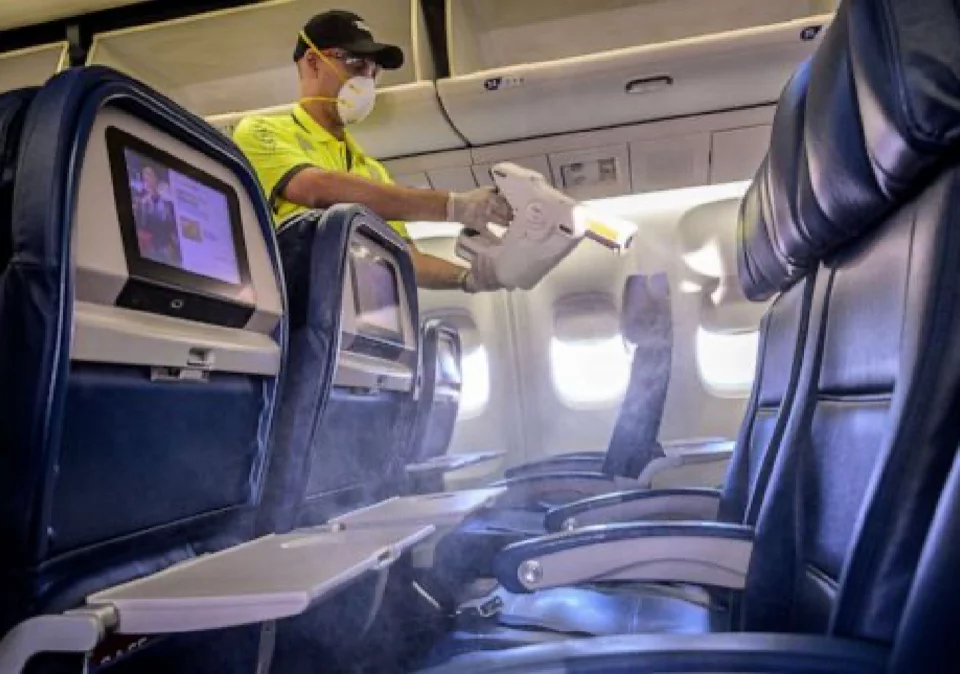 Man in mask uses electrostatic sprayer on airplane seats